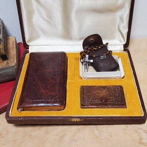 May include: A brown leather-bound box with a yellow satin lining. The box contains a brown leather wallet, a small brown leather pouch with a silver cross and brown beads, and a small brown leather coin purse.