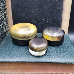 May include: Three round, decorative boxes made of horn. The boxes are different sizes and have a mottled brown and yellow pattern.