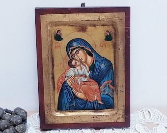 Puede incluir: Un icono enmarcado en madera que representa a la Virgen María sosteniendo al niño Jesús. El icono está pintado en un estilo tradicional con detalles dorados. El icono está rodeado de un fondo dorado y un marco de madera oscura.