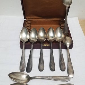 May include: A set of nine silver spoons in a brown leather case. The spoons are all the same size and shape, with a rounded bowl and a long, slender handle. The case has a velvet lining and a hinged lid.