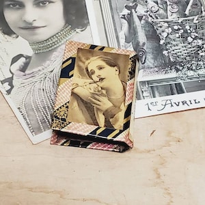 May include: A vintage matchbox with a colorful striped design. The front of the box features a black and white image of a woman holding a cigarette.
