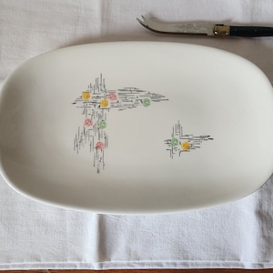 Puede incluir: Plato de servir ovalado blanco con un diseño geométrico en blanco y negro y puntos de colores. El plato está sobre un mantel blanco.