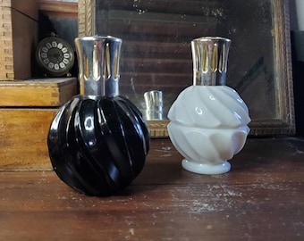 Könnte beinhalten: Zwei dekorative Öllampen-Flaschen, eine schwarze und eine weiße, mit einem Spiralmuster. Beide Flaschen haben einen silbernen Deckel mit goldener Verzierung.