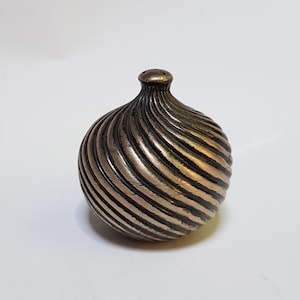 Può includere: Un piccolo saliera rotondo in ceramica dorata e nera con un design a spirale.