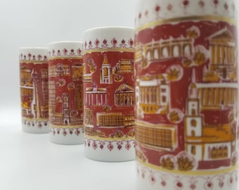 May include: Four white ceramic mugs with red and gold designs featuring cityscapes. The mugs have a decorative border around the top.