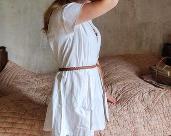 May include: A short white dress with short sleeves and a scalloped edge detail. The dress features a thin, braided brown leather belt cinched at the waist. The fabric has a subtle vertical texture and a loose, flowing fit that falls above the knee.
