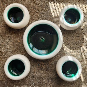 May include: Five white ceramic bowls with a green interior. The bowls are round and have a smooth, glossy finish.
