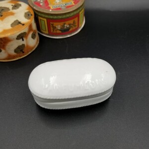 Può includere: Scatola portaoggetti ovale in ceramica bianca con un design in rilievo attorno al bordo. La scatola è chiusa.