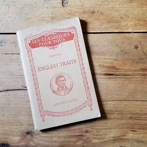 May include: A vintage book titled "English Traits" by Emerson. The book is part of a series called "Les Classiques Pour Tous" and features a red illustration of the author on the cover.
