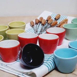 May include: A set of 10 small ceramic bowls in various colors, including green, red, and blue, with wooden skewers. The bowls are arranged on a white and green striped towel.