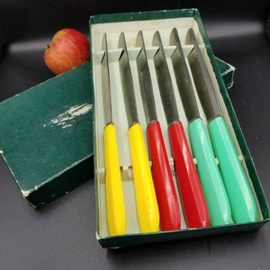 Peut inclure: Ensemble de six couteaux à beurre avec des manches colorés dans une boîte verte. Les manches sont jaunes, jaunes, rouges, rouges et verts.