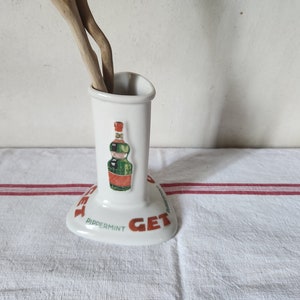 Può includere: Portautensili in ceramica bianca con una grafica di una bottiglia di liquore alla menta verde e rossa e il testo "GET Peppermint GET".