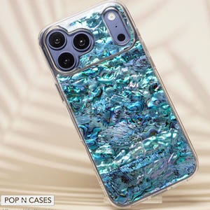 May include: A clear phone case featuring a shimmering, iridescent blue and green abalone shell design. The case has a clear border and covers the phone's camera lenses. The phone case is angled slightly, showcasing the design.