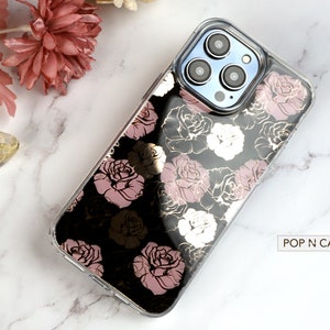 May include: A clear phone case with a black background and a rose pattern in gold and pink. The case is designed for a phone with a triple camera lens. The text "POP N CASES" is visible in the bottom right corner of the image.