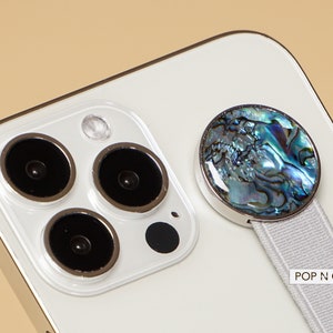 May include: A white iPhone with a pop socket featuring a blue and green iridescent shell design. The text "POP N CASES" is printed on the white phone case.
