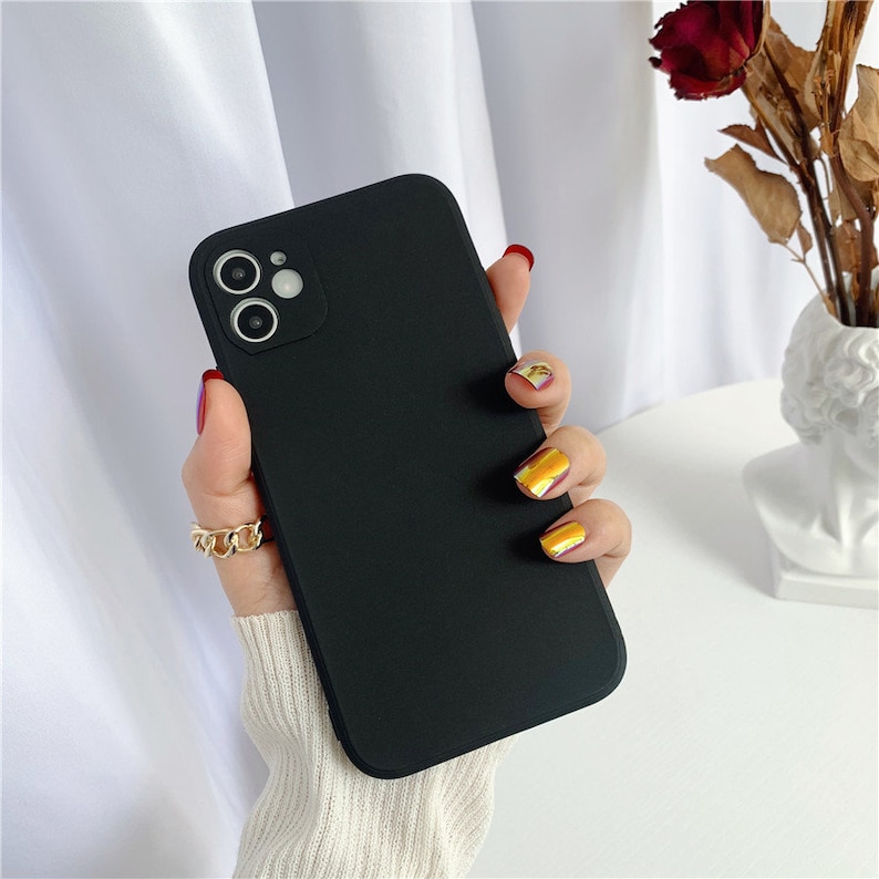 May include: A black phone case with a camera cutout. The case is being held by a hand with gold nail polish.