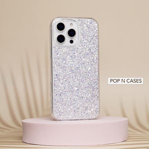 May include: A clear phone case with a sparkly silver glitter design. The case is designed for an iPhone and has a cutout for the camera lens. The text "POP N CASES" is visible in the image.
