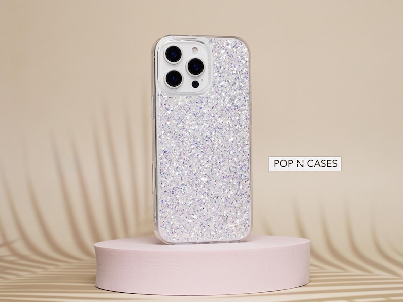 May include: A clear phone case with a sparkly silver glitter design. The case is designed for an iPhone and has a cutout for the camera lens. The text "POP N CASES" is visible in the image.