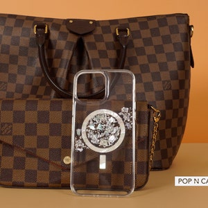 May include: A clear phone case with a silver glitter design and a white circle in the center. The case is sitting on top of a brown and white checkered purse. The text "POP N CASES" is visible in the bottom right corner of the image.