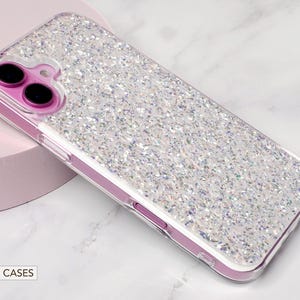 May include: A clear phone case with a sparkly iridescent glitter design. The case is designed for an iPhone and has a raised camera bump.