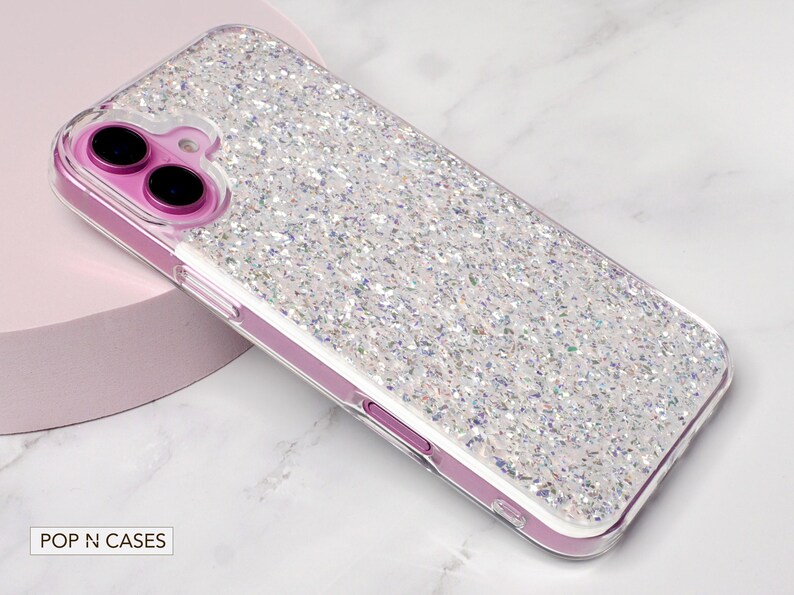 May include: A clear phone case with a sparkly iridescent glitter design. The case is designed for an iPhone and has a raised camera bump.