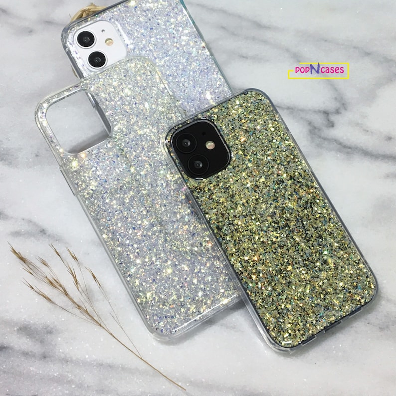 May include: Two glitter phone cases, one silver and one gold, with a clear back and a raised camera bump. The cases are on a white marble surface. The text "popNcases" is visible in the top right corner of the image.