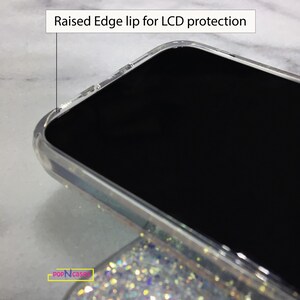 May include: Close-up of a clear phone case with a raised edge lip for LCD protection. The case is on a sparkly background.