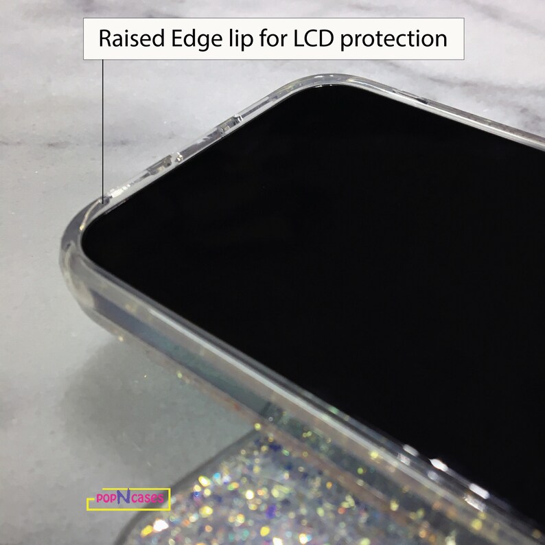 May include: Close-up of a clear phone case with a raised edge lip for LCD protection. The case is on a sparkly background.
