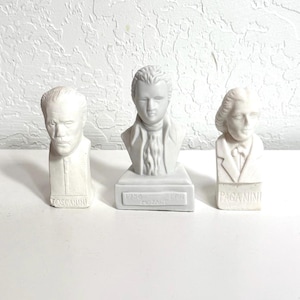 Può includere: Tre busti in ceramica bianca di personaggi storici. Il busto a sinistra reca la scritta "TOSCANINI". Il busto centrale reca la scritta "1756 MOZART 1791". Il busto a destra reca la scritta "PAGANINI".