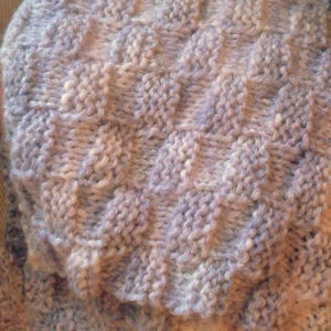 K&ouml;nnte beinhalten: Nahaufnahme eines gestrickten Stoffes mit einem strukturierten Muster. Der Stoff ist helllila mit einer dezenten wei&szlig;en Variation.
