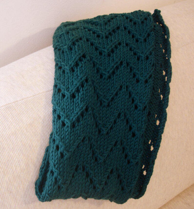 May include: A dark green knitted blanket with a lacy pattern. The blanket is folded and draped over a white couch.