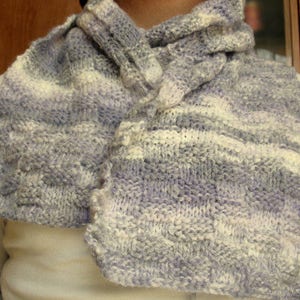 K&ouml;nnte beinhalten: Ein weicher, gestrickter Schal in Wei&szlig;-, Grau- und Lilat&ouml;nen. Der Schal ist aus einem dicken Garn gefertigt und hat eine strukturierte, gewebte Optik.