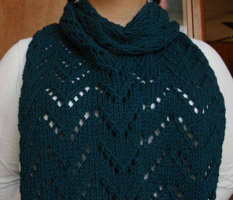 May include: A teal blue knitted scarf with a lacy pattern. The scarf is folded over and has a loose, flowing style.
