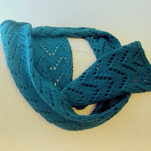 May include: A teal blue knitted scarf with a lacy pattern. The scarf is folded in half and draped over a white surface.
