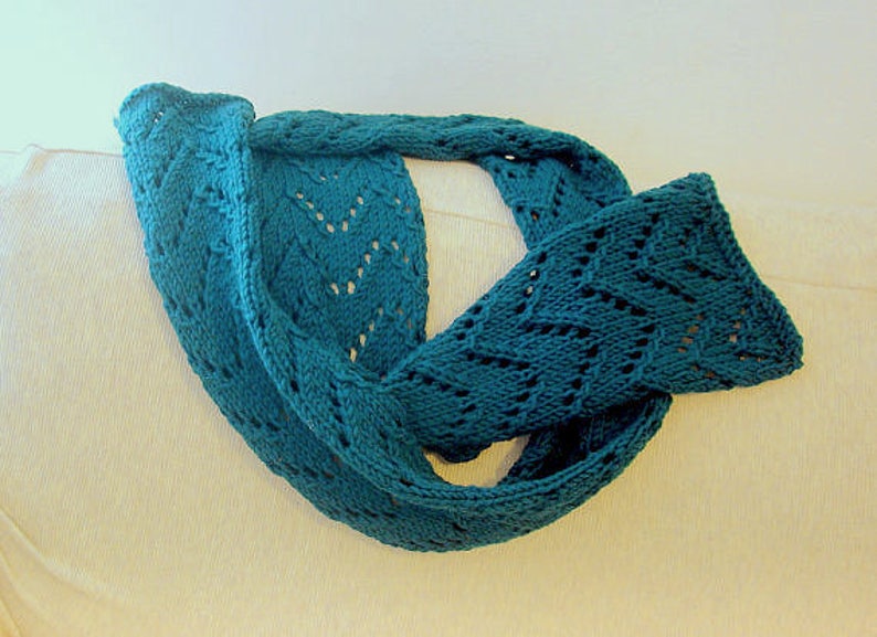 May include: A teal blue knitted scarf with a lacy pattern. The scarf is folded in half and draped over a white surface.