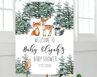 May include: A baby shower welcome sign featuring woodland animals and evergreen trees. The sign reads "Welcome to Baby Elijah's Baby Shower 1/12/2020" in elegant script. The sign is displayed on a wooden easel.