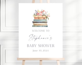 May include: A white sign with a stack of books and flowers on top. The sign says "Welcome to Stephanie's Baby Shower June 30, 2024".