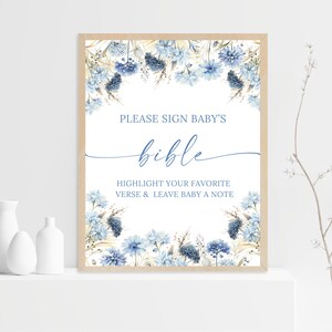 May include: A framed sign with the text "PLEASE SIGN BABY'S bible" in blue script. The sign is decorated with blue floral accents and the text "HIGHLIGHT YOUR FAVORITE VERSE & LEAVE BABY A NOTE".