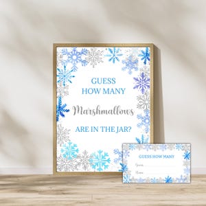 May include: A framed sign and matching cards with a winter theme. The sign reads "Guess How Many Marshmallows Are in the Jar?" in blue and silver text, surrounded by blue and silver snowflakes. The cards have the same design.