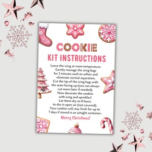 Pode incluir: Uma folha de instruções festiva para um kit de biscoitos, com ilustrações rosa e brancas de biscoitos e enfeites de Natal. O texto "COOKIE KIT INSTRUCTIONS" é exibido de forma proeminente, com etapas detalhadas para decorar biscoitos. As palavras "Merry Christmas!" estão na parte inferior.