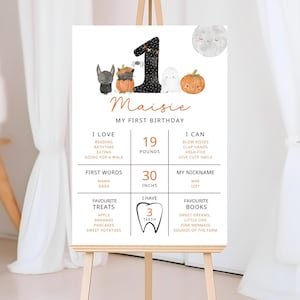 Puede incluir: Un póster blanco sobre un caballete con el texto "Maisie, My First Birthday". El póster incluye un número 1, ilustraciones temáticas de Halloween y detalles sobre los gustos del niño, sus primeras palabras y sus cosas favoritas. El póster mide 76 cm de altura.