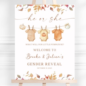 May include: A gender reveal sign featuring watercolour autumn leaves, pumpkins, and three baby onesies hanging on a clothesline. Text reads: he or she, WHAT WILL OUR LITTLE PUMPKIN BE?, WELCOME TO Brooke & Julian's GENDER REVEAL, OCTOBER 19, 2025.