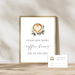 Pode incluir: Uma placa emoldurada com o texto "GUESS HOW MANY coffee beans ARE IN THE JAR?" e um cartão menor correspondente. A placa apresenta uma imagem em aquarela de uma xícara de café com um desenho de coração na espuma e vegetação.
