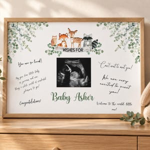May include: A framed print featuring a central ultrasound image, watercolor illustrations of a forest owl, fox, deer, and raccoon, and the text "WISHES FOR" and "Baby Asher" surrounded by eucalyptus leaves and handwritten-style messages.