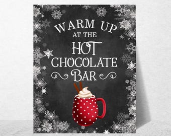 May include: A rectangular sign with a black chalkboard background featuring white snowflake illustrations along the border. The text reads WARM UP AT THE HOT CHOCOLATE BAR above a red mug with white polka dots, whipped cream, and two cinnamon sticks.