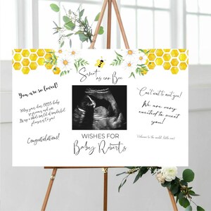 Puede incluir: Un cartel blanco con un patrón de panal de abeja amarillo y una ilustración de abeja. El cartel dice "Sweet as can Bee" y tiene una imagen de sonograma con el texto "Wishes for Baby Roberts". El cartel también incluye el texto "You are so loved!" y "Can't wait to meet you!"