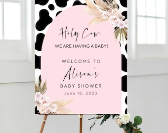 May include: A pink and white baby shower welcome sign with a cow print background. The sign says "Holy Cow We Are Having A Baby! Welcome To Alison's Baby Shower June 18, 2023".