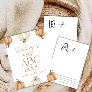 Peut inclure: Ensemble de trois cartes en papier blanc avec des illustrations sur le thème de l'automne. La carte principale indique "Baby's First ABC Book" en lettres dorées, ornée de citrouilles à l'aquarelle. Deux cartes plus petites présentent les lettres "A" et "B" avec des lignes pour écrire.