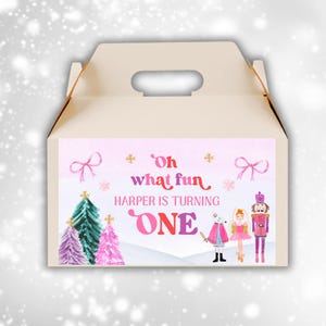 May include: A beige party favor box with a handle, featuring a pink and white label. The label reads "Oh what fun, Harper is turning ONE" with illustrations of Christmas trees, bows, and characters.