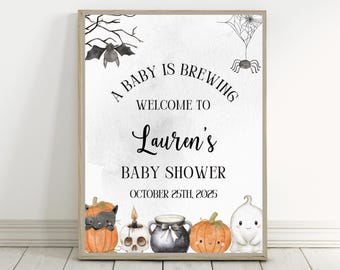 May include: A framed baby shower sign with a Halloween theme. The sign reads "A Baby is Brewing" and welcomes guests to Lauren's baby shower on October 25th, 2025. The sign features illustrations of a bat, spider, pumpkins, and a ghost.
